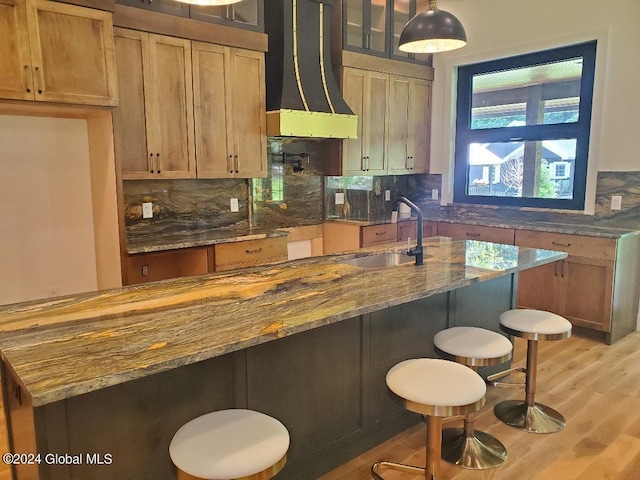 kitchen featuring sink, premium range hood, backsplash, light stone countertops, and decorative light fixtures