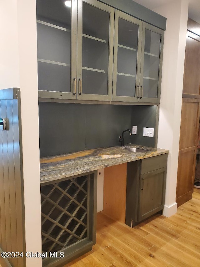 bar featuring light hardwood / wood-style floors, sink, and stone counters