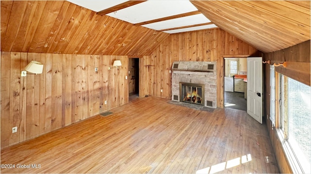 unfurnished living room featuring vaulted ceiling with beams, a fireplace, wood walls, and light wood-type flooring