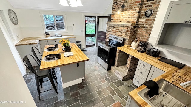 67 Adams Ln, Schroon, NY 12870 - kitchen with butcher block countertops, stainless steel electric range oven, a chandelier, crown molding, and brick patterned floors