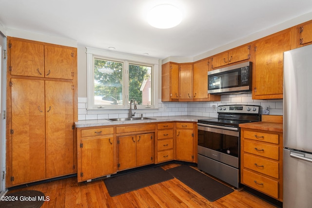 kitchen featuring sink, backsplash, stainless steel appliances, and light wood-type flooring