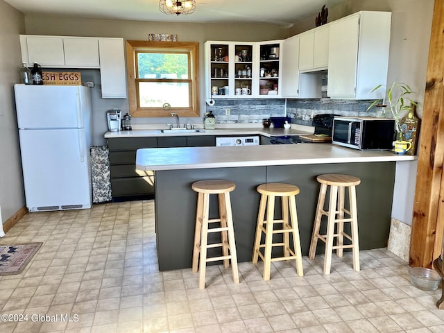 kitchen with a breakfast bar, white appliances, sink, kitchen peninsula, and white cabinetry