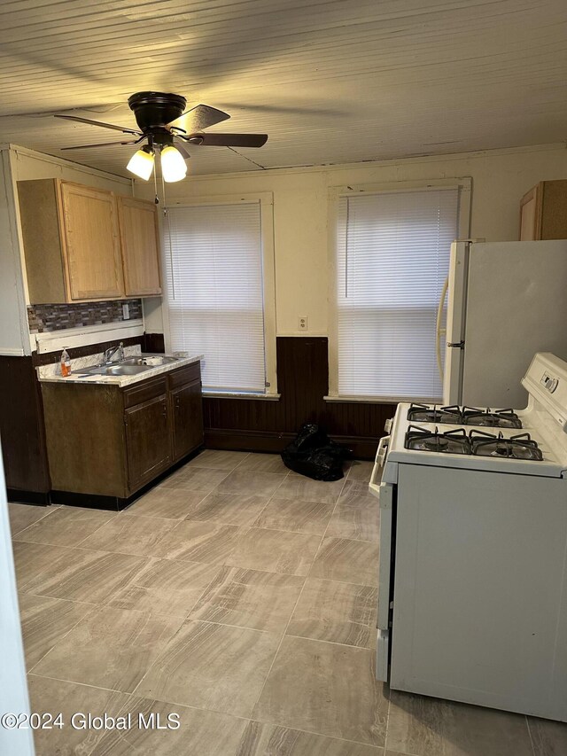 kitchen featuring sink, white appliances, ceiling fan, and wood walls