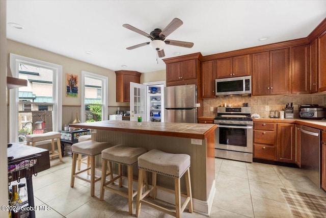 kitchen with light tile patterned flooring, tile counters, backsplash, ceiling fan, and stainless steel appliances