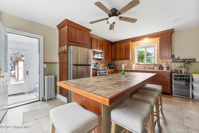 kitchen featuring tasteful backsplash, wine cooler, radiator heating unit, stainless steel appliances, and tile countertops