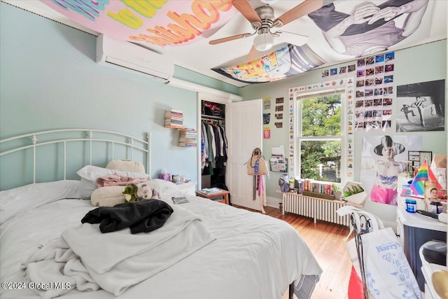 bedroom featuring a closet, ceiling fan, radiator heating unit, hardwood / wood-style floors, and a wall unit AC