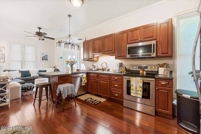 kitchen featuring dark wood-type flooring, ceiling fan, appliances with stainless steel finishes, decorative light fixtures, and a kitchen bar