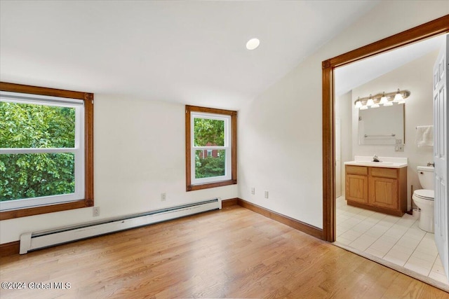 unfurnished bedroom featuring a baseboard heating unit, light hardwood / wood-style floors, multiple windows, and ensuite bath