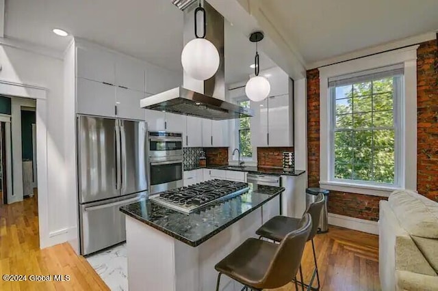 kitchen with island exhaust hood, appliances with stainless steel finishes, a wealth of natural light, and decorative light fixtures