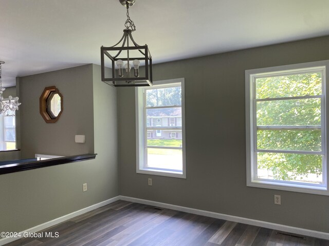 spare room with dark wood-type flooring, a wealth of natural light, and an inviting chandelier