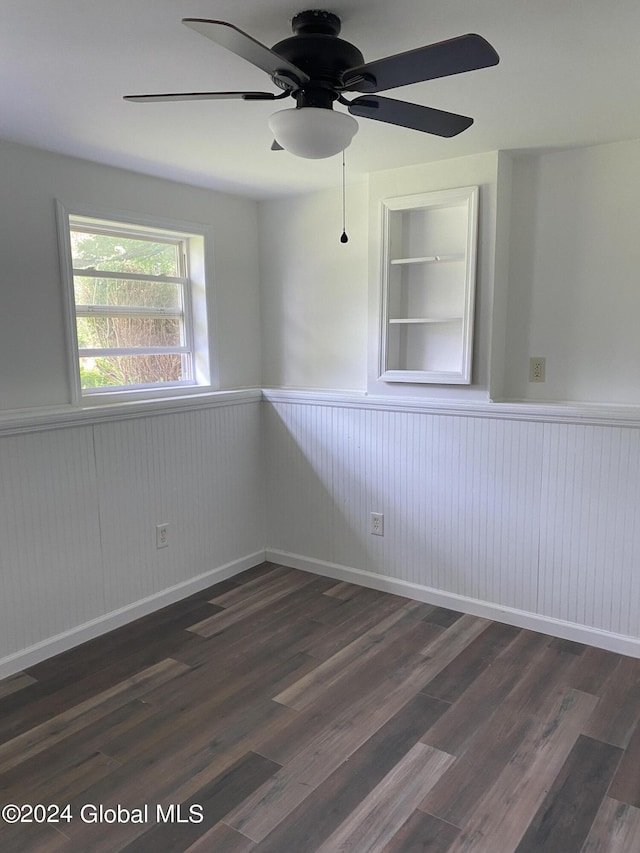 unfurnished room with built in features, dark wood finished floors, a ceiling fan, and wainscoting