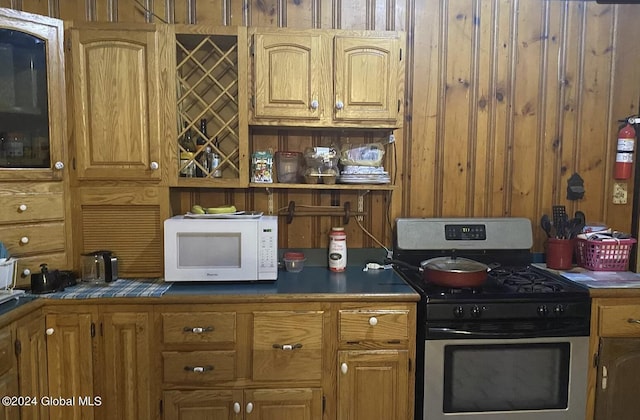 kitchen featuring dark countertops, white microwave, gas stove, and wooden walls