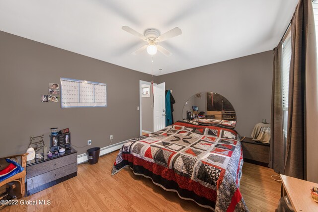 bedroom with light wood-type flooring, ceiling fan, and a baseboard heating unit