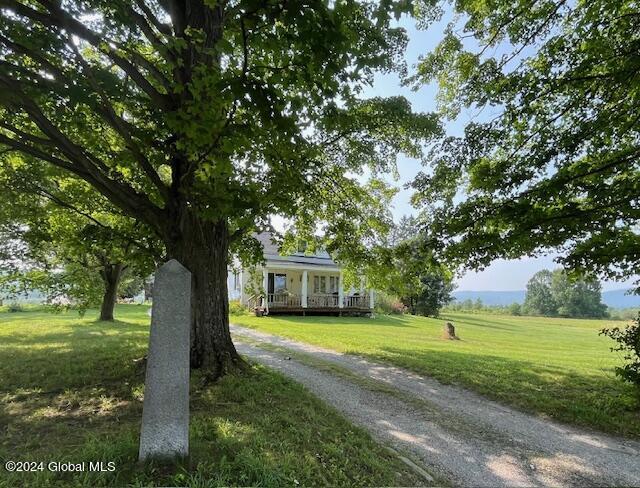 view of front of home with a porch, a front yard, and a rural view