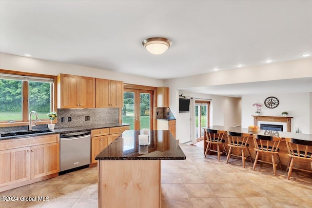 kitchen featuring dark stone counters, sink, light tile patterned floors, a kitchen island, and dishwasher