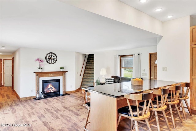 kitchen featuring dark stone counters, a premium fireplace, light wood-type flooring, and a kitchen bar