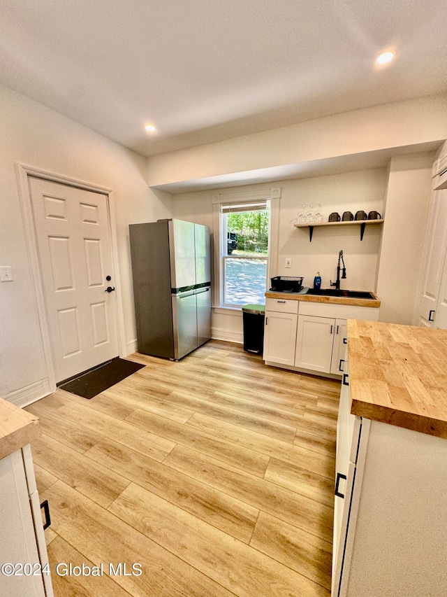 kitchen with wood counters, white cabinets, sink, stainless steel refrigerator, and light wood-type flooring