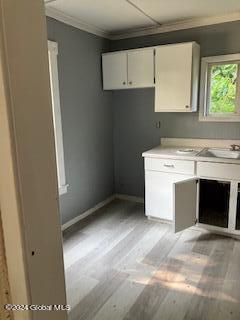 kitchen featuring white cabinetry, ornamental molding, sink, and light hardwood / wood-style flooring