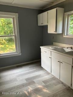 kitchen with white cabinetry, sink, crown molding, and light hardwood / wood-style flooring