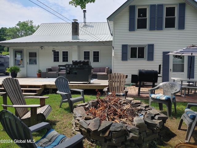 rear view of property with metal roof, a chimney, an outdoor living space with a fire pit, and a deck