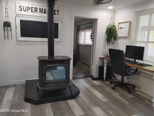 home office featuring wood finished floors, ornamental molding, and a wood stove