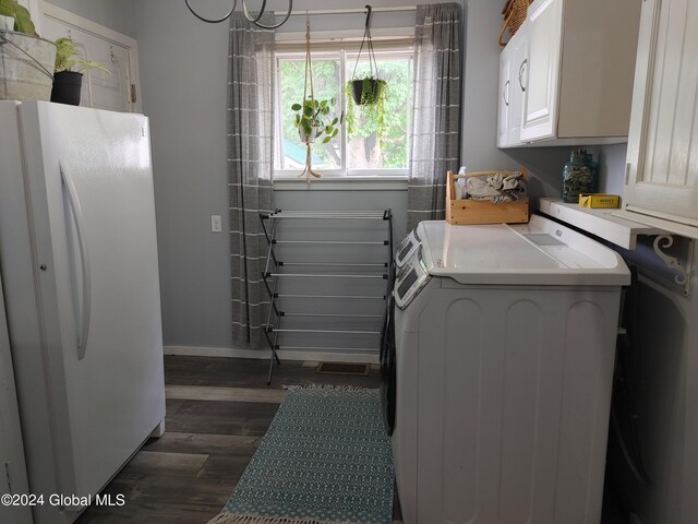 laundry room with dark wood-type flooring, washing machine and dryer, and cabinets