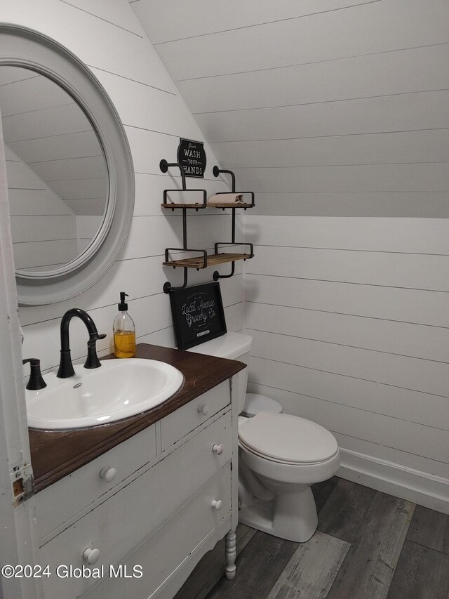 bathroom featuring wooden walls, toilet, vanity, hardwood / wood-style floors, and vaulted ceiling