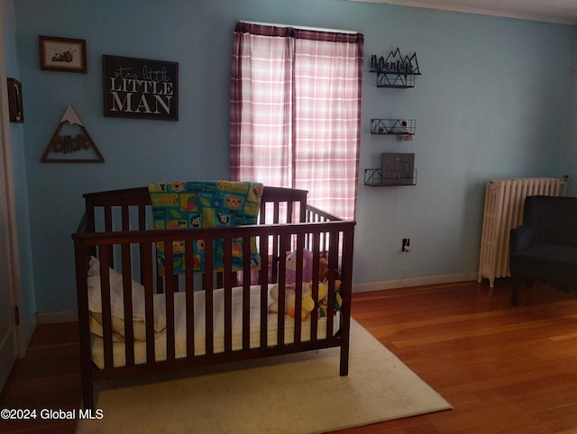 bedroom featuring a crib, radiator, wood finished floors, and baseboards