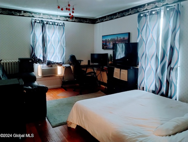 bedroom with cooling unit, radiator, wood finished floors, and wallpapered walls