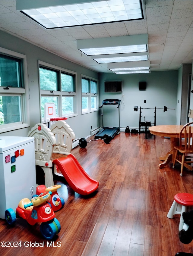 recreation room featuring a paneled ceiling, wood finished floors, and a wall unit AC