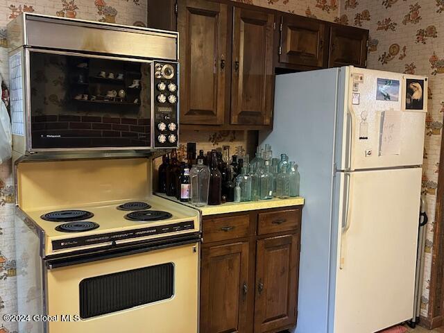 kitchen with light countertops, white appliances, dark brown cabinetry, and wallpapered walls