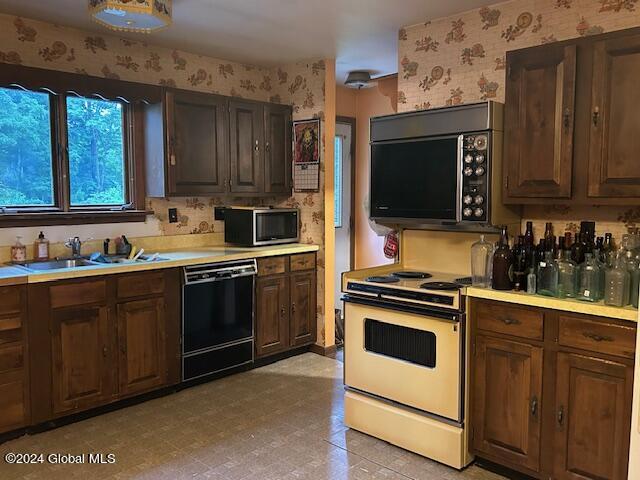 kitchen with dark brown cabinetry, wallpapered walls, light countertops, black appliances, and a sink