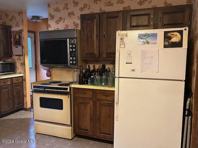 kitchen with stainless steel microwave, freestanding refrigerator, range with electric cooktop, black microwave, and wallpapered walls