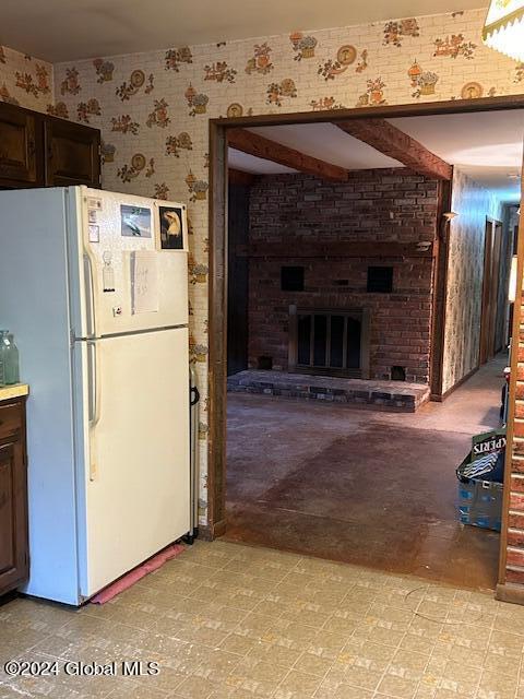 interior space featuring dark brown cabinets, a brick fireplace, freestanding refrigerator, light floors, and wallpapered walls