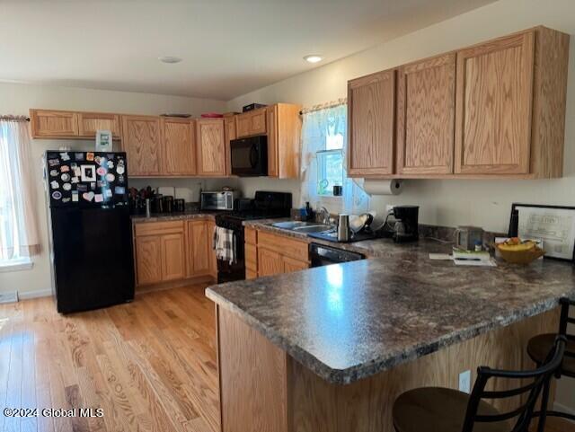 kitchen with a kitchen breakfast bar, kitchen peninsula, black appliances, and a healthy amount of sunlight