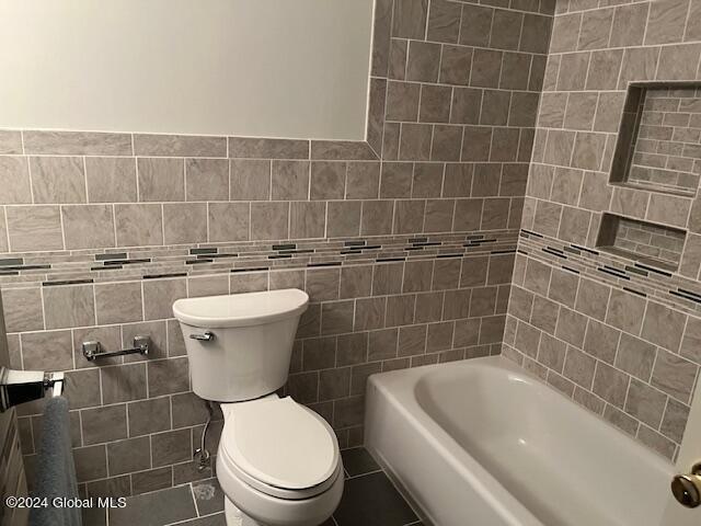 bathroom featuring shower / washtub combination, tile walls, and toilet