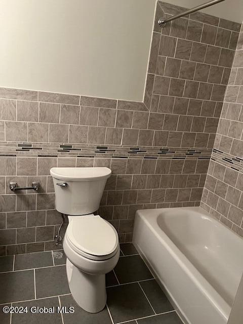 bathroom with tile patterned floors, toilet, tiled shower / bath combo, and tile walls