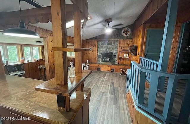 kitchen with hardwood / wood-style flooring, ceiling fan, a fireplace, vaulted ceiling, and wood walls