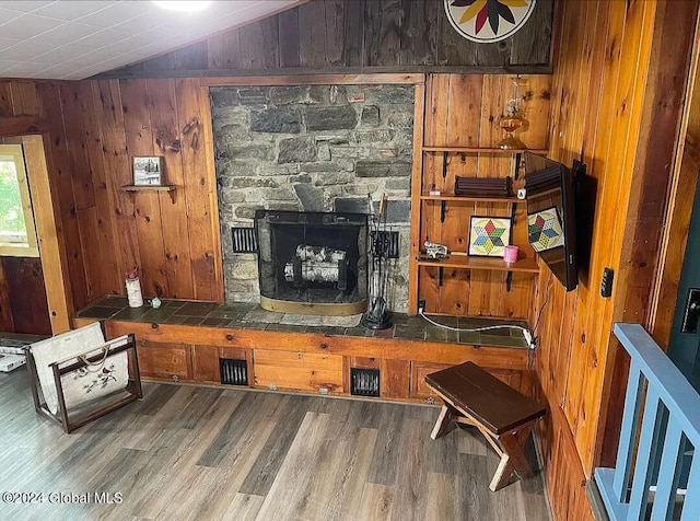 living room with vaulted ceiling, a stone fireplace, hardwood / wood-style floors, and wood walls