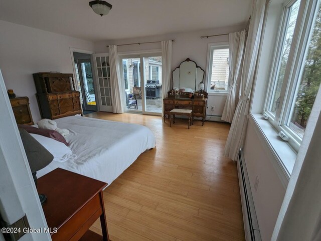 bedroom with a baseboard heating unit, access to exterior, and light wood-type flooring