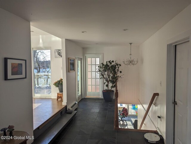 hall with a baseboard radiator, a chandelier, dark tile patterned flooring, and a wealth of natural light