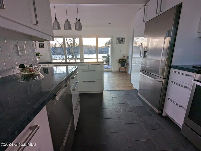 kitchen featuring dishwashing machine, stainless steel refrigerator, dark tile patterned flooring, backsplash, and dark stone countertops