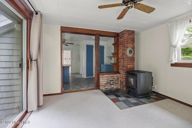 carpeted living room featuring ceiling fan, a wood stove, and brick wall