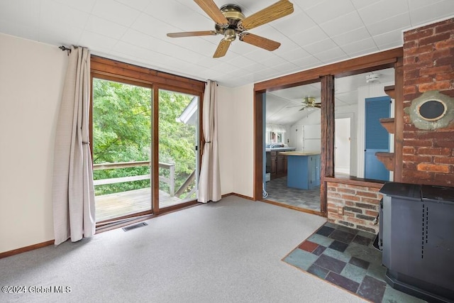 unfurnished living room featuring ceiling fan, a drop ceiling, brick wall, and a wood stove