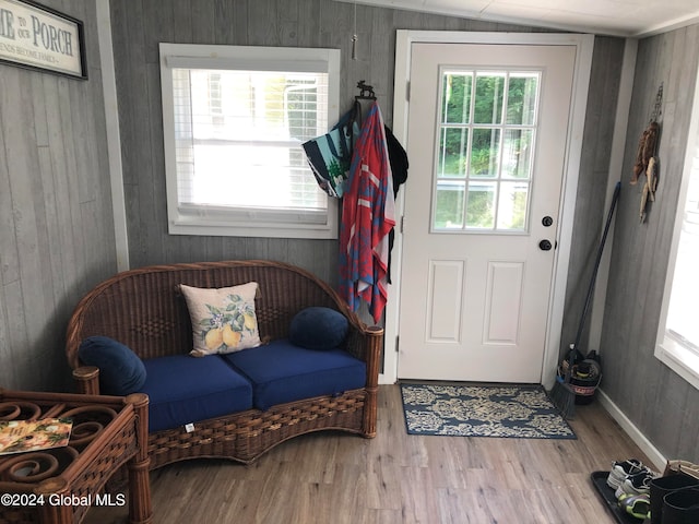 doorway with hardwood / wood-style floors, wooden walls, and vaulted ceiling