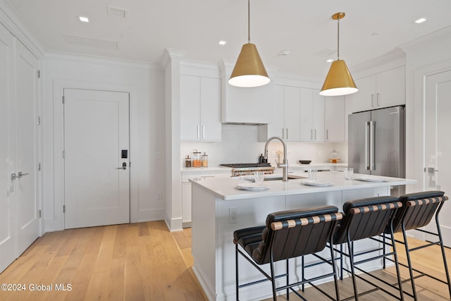 kitchen with a breakfast bar, a sink, light countertops, high end refrigerator, and crown molding