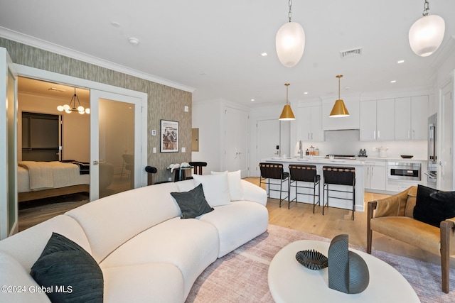 living area featuring visible vents, light wood finished floors, wallpapered walls, crown molding, and a chandelier