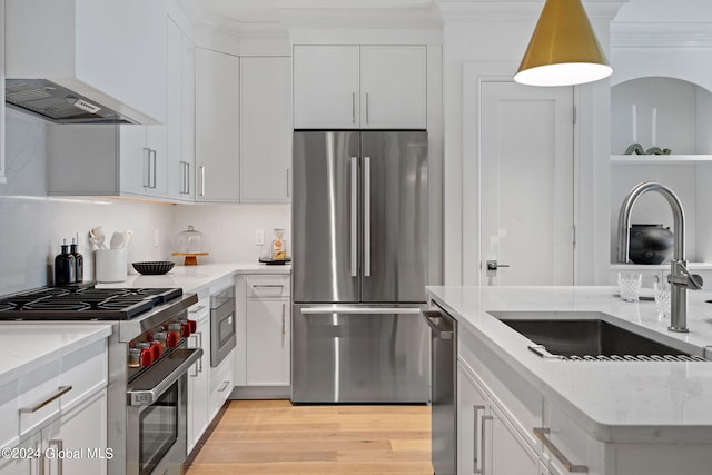 kitchen with light wood-style flooring, a sink, stainless steel appliances, wall chimney exhaust hood, and white cabinets