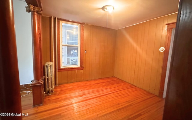 empty room with wooden walls, light hardwood / wood-style flooring, and radiator heating unit