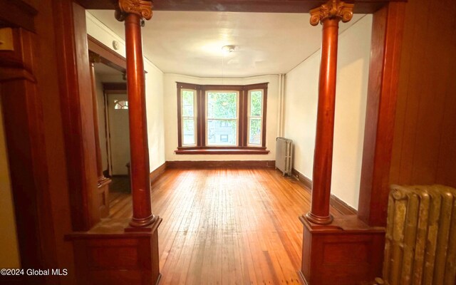 corridor with radiator, hardwood / wood-style floors, and ornate columns